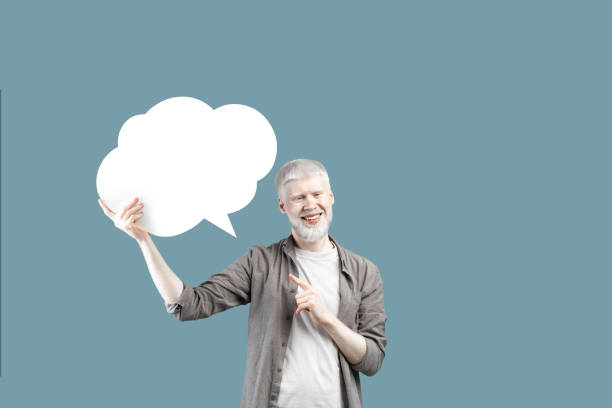 istock Excited young albino man pointing at empty speech bubble, standing over blue studio background, mockup for design 1326430368