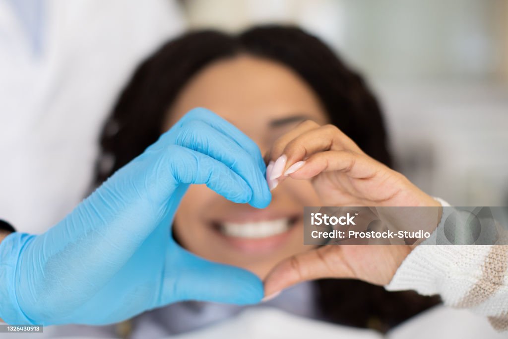 Closeup Of Dentist Doctor And Female Patient Making Heart Gesture With Hands Closeup Shot Of Dentist Doctor And Female Patient Making Heart Gesture With Hands, Professional Stomatologist Wearing Blue Medical Glove, Black Lady Happy With Successful Teeth Treatment, Cropped Dentist Stock Photo