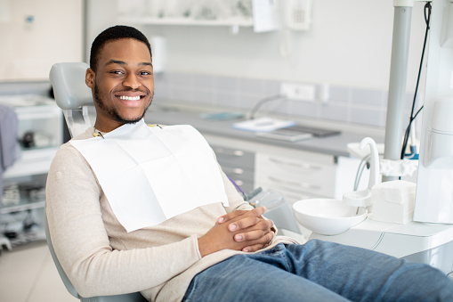 Dental Clinic Concept. Portrait Of Joyful Young Black Guy Sitting In Chair Iin Stomatological Cabinet, Millennial African American Man Ready For Checkup And Medical Treatment With Dentist, Copy Space