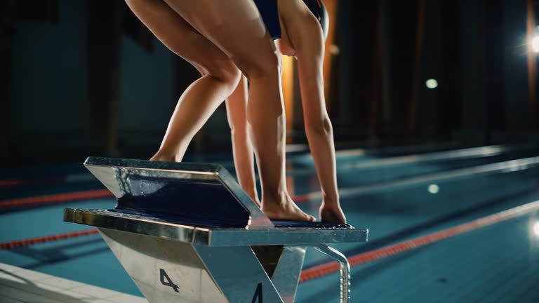 Athletic Female Swimmer Comes to Starting Block, Ready to Dive into Swimming Pool. Professional Woman Athlete Ready to Win Championship. Cinematic Light, Stylish Colors, Back View Following Arc Shot
