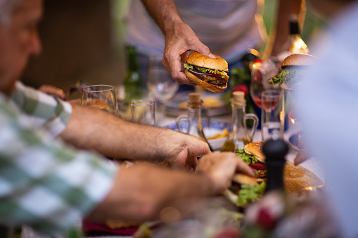 Group of senior friends eating burgers during dinner party at backyard