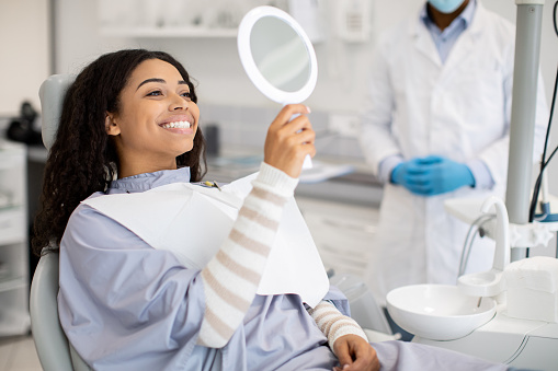 Paciente femenina negra feliz mirando el espejo después del tratamiento dental en la clínica photo