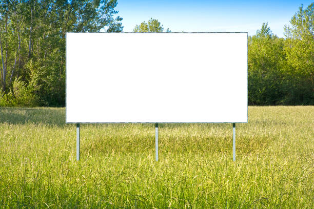 istock Blank advertising signboard in a green field with trees on background - concept with copy space 1326440361