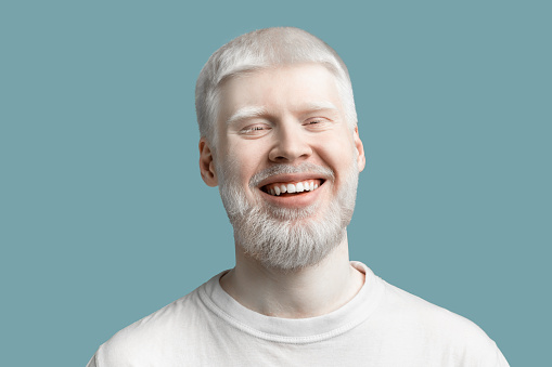 Retrato de hombre albino barbudo feliz con piel pálida y pelo blanco sonriendo a la cámara sobre fondo turquesa photo