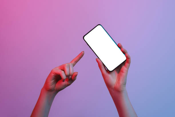 istock A phone with a white, blank screen in a woman's hand on a gradient background. Pointing her finger at the phone. 1326444022