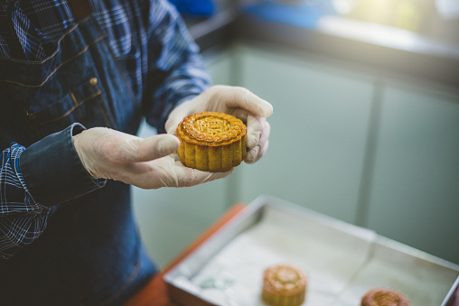 An Asian male baker put homemade Chinese holding a mooncake ready placed on gold-colored plastic container, ready to be pack and delivery. Support local small business concept.