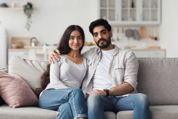 istock Young muslim couple sitting on couch and looking at camera 1326447330