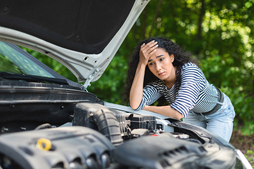 Sad brunette woman leaning on car hood, experiencing broken engine while car trip, waiting for auto service, closeup. Depressed young lady having troubles with her car, waiting for help