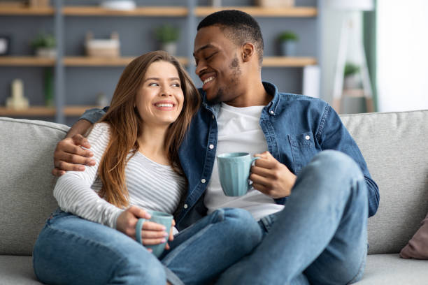 istock Happy Young Interracial Couple Drinking Coffee And Hugging On Couch At Home 1326449811
