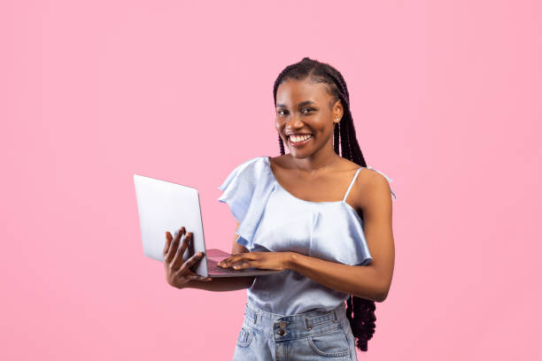 istock Young African American woman with afro bunches using laptop computer, working or studying online on pink background 1326449857