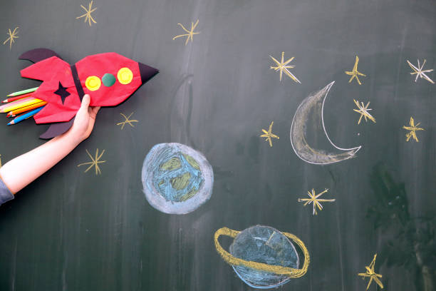 istock Child hand with selfmade red rocket and school blackboard. 1326450185