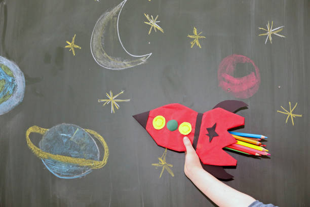 istock Child hand with selfmade red rocket and school blackboard. 1326450192