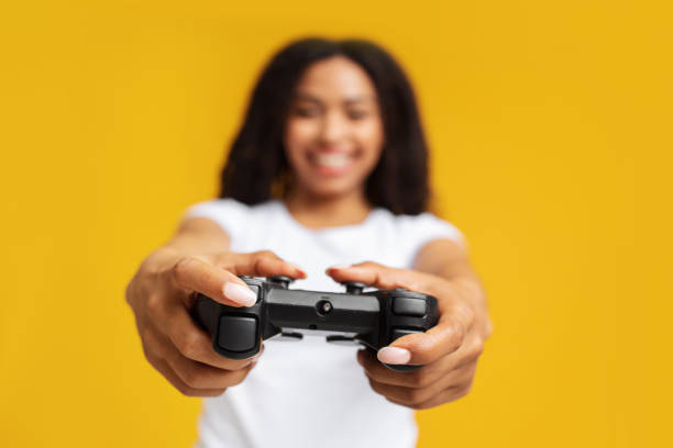 istock New videogame advertisement concept. Overjoyed african american woman holding game controller, yellow background 1326451157