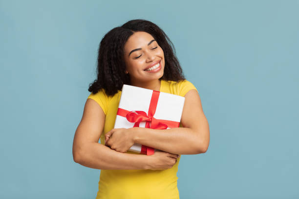 istock Best present. Joyful african american lady hugging gift box posing over blue studio background, smiling with closed eyes 1326451706