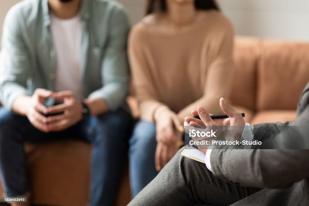 Couple talking at session with male therapist Help Concept. Closeup Cropped View Of Male Counselor Therapist Or Consultant In Suit Talking With Couple Sitting In Office, Giving Professional Advice. Selective Focus On Hands With Clipboard And Pen Psychotherapy Stock Photo