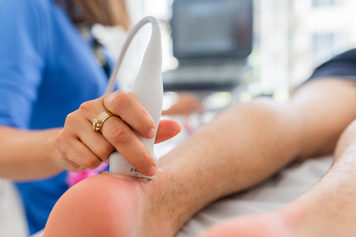 Close up of a woman's hand doing an ultrasound of the Achilles tendon on a patient as he lies on an examination table in the office.