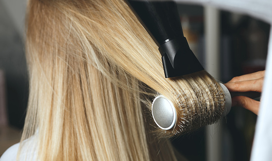 Hair stylist drying client's hair with a brush comb and a hair dryer at beauty salon