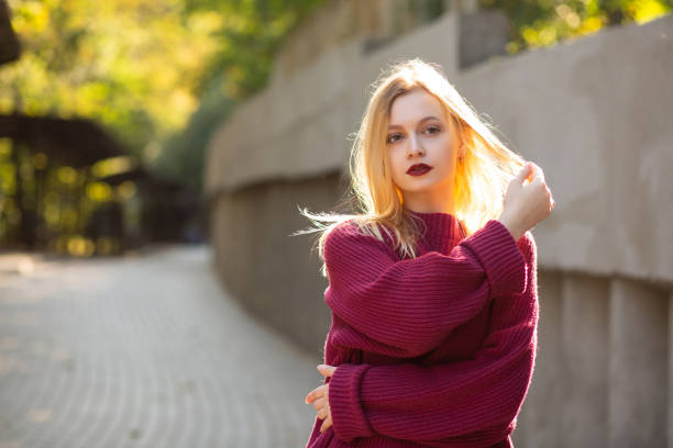 istock Elegant blonde model with red lips wearing red oversize sweater posing in rays of sun. Empty space 1326455771