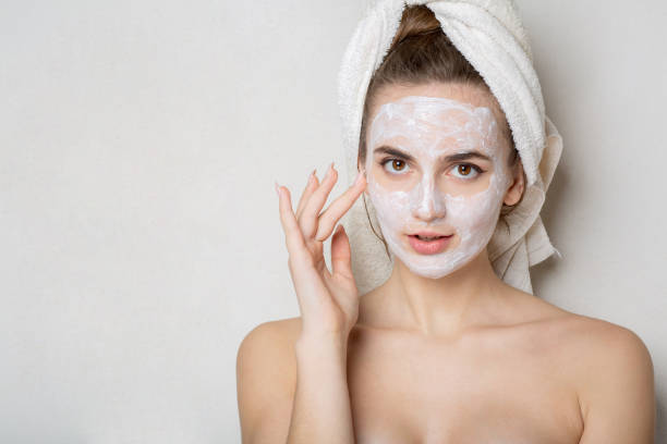 istock Adorable woman with bath towel on head using cream mask 1326457133