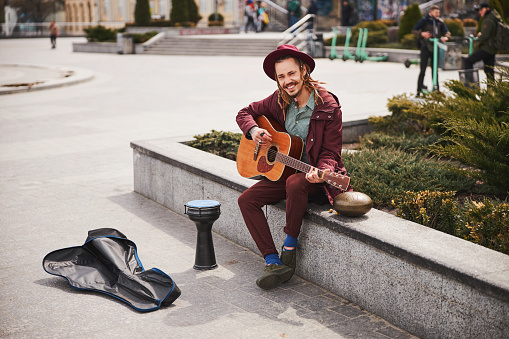 Kind street musician sitting on the border while demonstrating his smile and music