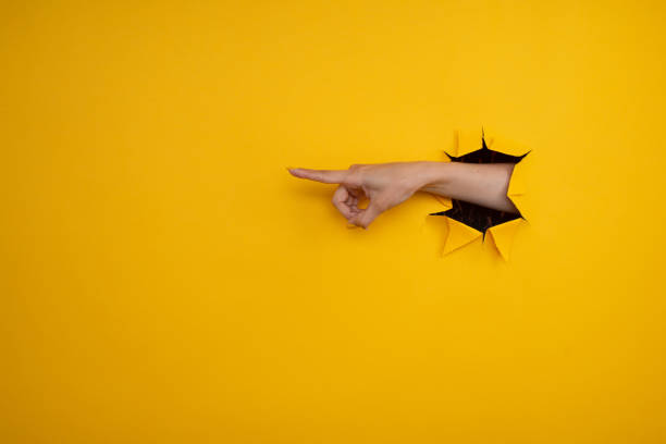 istock Hand point at something out of a hole in torn yellow paper. Left direction, gestures. 1326462504
