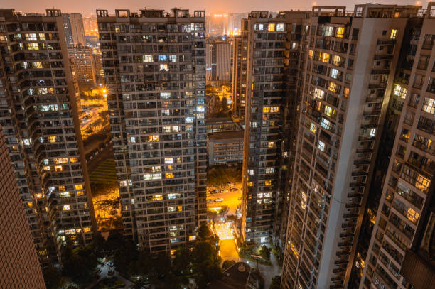 istock Long exposure night aerial view on residential buildings complex compound. Tall skyscrapers thousands of apartments light illuminates from windows. Small square park inside community. City development 1326462712
