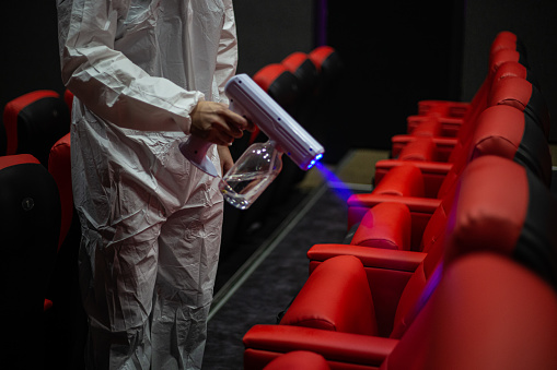Asian Chinese cinema Hygienist with Respirator Mask performing disinfection in cinema hall on chairs and carpet before the movie show time