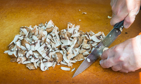 A man, wearing plastic gloves chops mushrooms on a wooden cutting board in preparation of fresh pizzas.