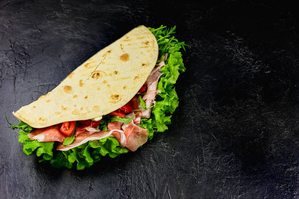istock piadina with salad, smoked ham, prosciutto on a black slate background 1326467587