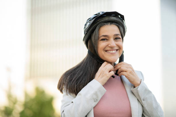 dość dojrzała kobieta biznesu stawia na kask rowerowy - senior adult outdoors physical activity mode of transport zdjęcia i obrazy z banku zdjęć