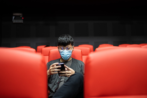 1 Asian Chinese man in an Empty Theater with protective mask surfing net using mobile.