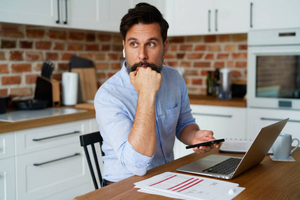 istock Man using phone with documents and laptop at home 1326471190