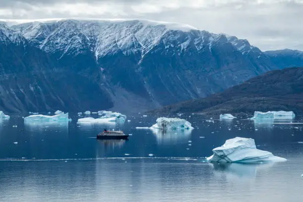 Photo of Seen from high on a hill, the expedition cruise ship MV Sea Spirit (Poseidon Expeditions) lies among several large icebergs, dwarfed by high, snow-dusted mountains in the background