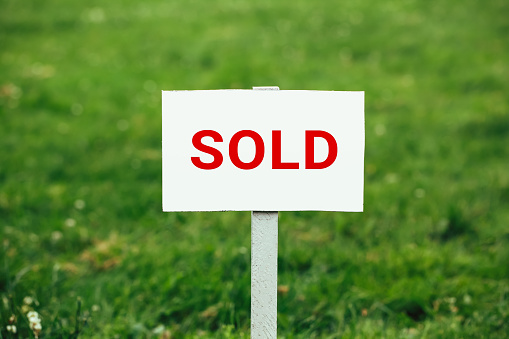 land sold plate sign, green grass background, close-up view