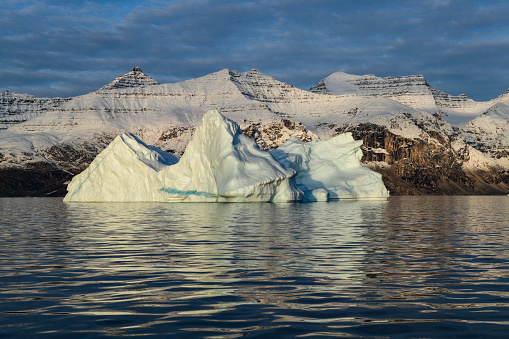 The peaks of a weathered iceberg bear a striking similarity to those of the snow-covered mountains in the background, Hekla Havn, Danmark Island, Scoresbysund, Sermersooq, East Greenland, Greenland, Europe