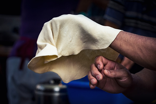 Close-up of chef hands tossing and stretching the pizza dough on concession stand.