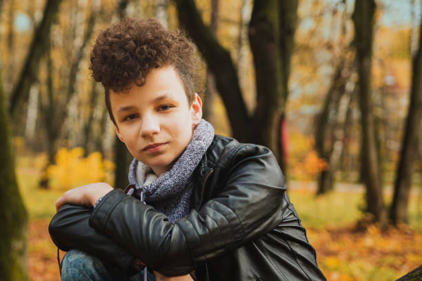 istock Curly brown-haired boy with a mohawk hairstyle in a leather jacket on an autumn background 1326482806