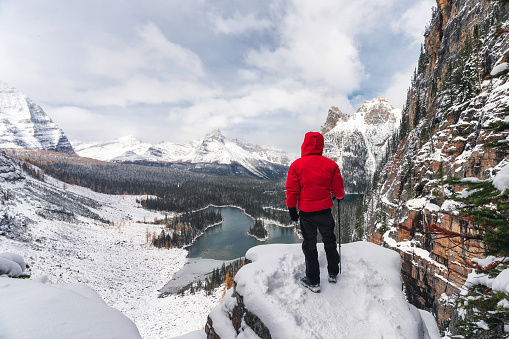 Traveler man in red winter coat standing and looking snowy mountain and lake view from Opabin Plateau peak at Yoho national park, Canada