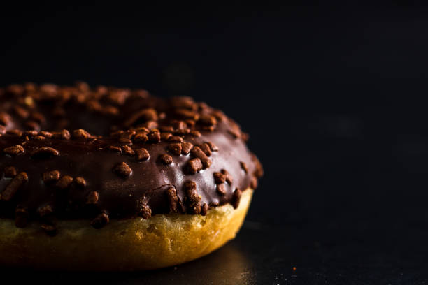 istock Fresh tasty colored donuts with sprinkles on black background 1326485957