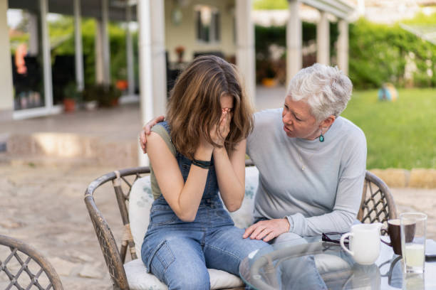 A grandmother comforts her upset grandchild A silver-haired grandmother has an arm around her granddaughter trying to comfort her as she is upset, holding her head in her hands and trying not to cry while they are both sitting outside on some garden furniture woman comforting depressed friend stock pictures, royalty-free photos & images