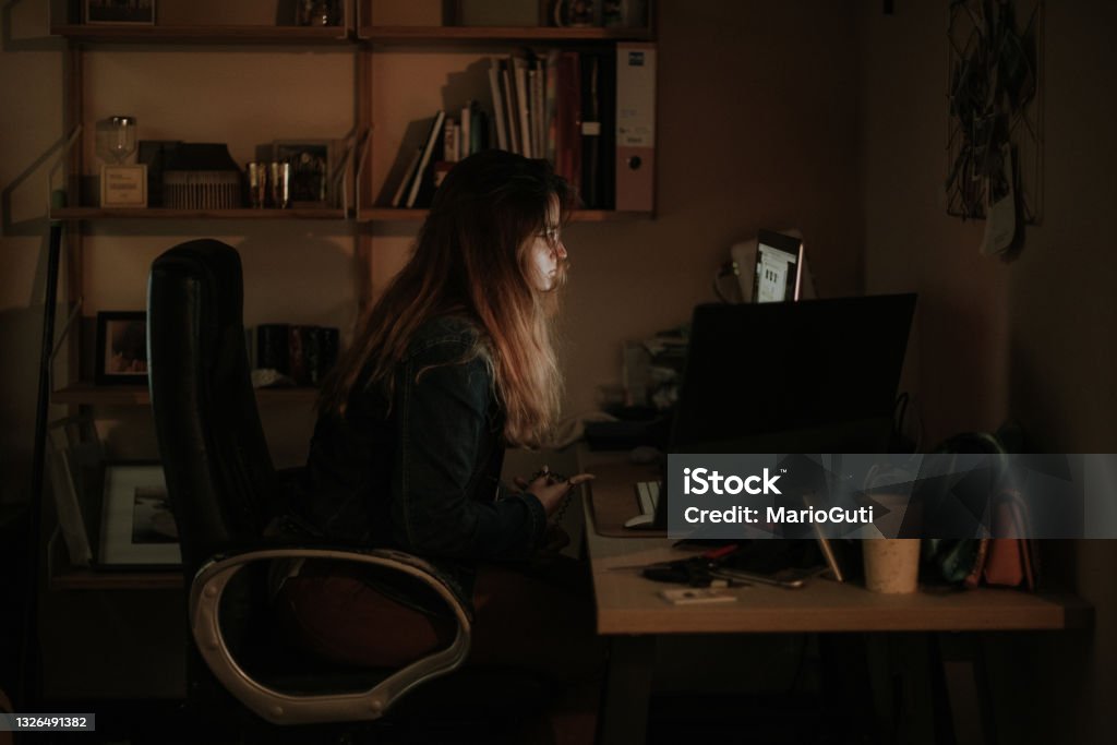 Young woman using computers in a dark room Side view of a young woman using computers in a dark room / office Darkroom Stock Photo