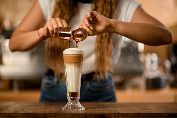 glass with syrup and whipped cream into which barista pours espresso from cups - espresso women cup drink imagens e fotografias de stock