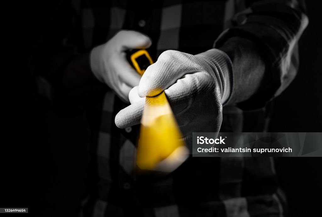 Male hands in white construction gloves holding yellow retractable tape measure tool and showing it forward to camera, closeup Male hands in white construction gloves holding yellow retractable tape measure tool and showing it forward to camera, closeup. Adhesive Tape Stock Photo