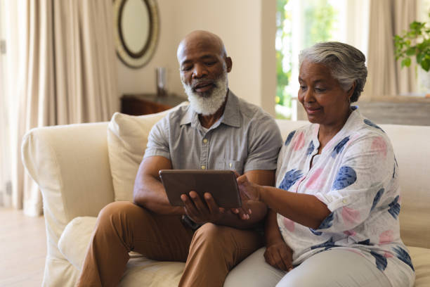 istock Senior african american couple sitting on sofa using tablet and smiling 1326494939