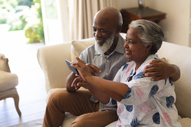 istock Senior african american couple sitting on sofa using smartphone taking selfies 1326495084