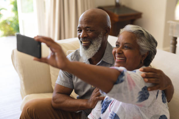 istock Senior african american couple sitting on sofa using smartphone taking selfies 1326495089