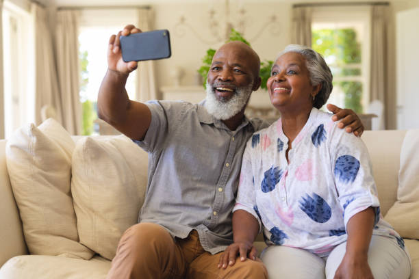 istock Senior african american couple sitting on sofa using smartphone taking selfies 1326495140