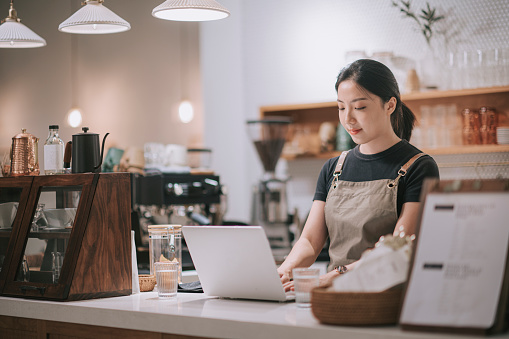 asian chinese female barista using laptop while enjoying dinner at coffee shop bar counter