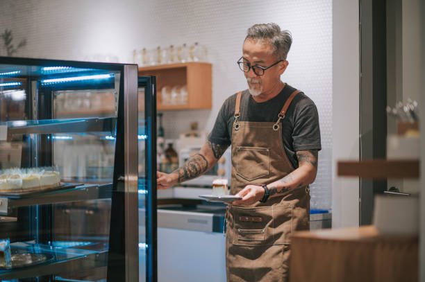 asian chinese senior man retrieving slice of cake dessert to serve to his customer from kitchen counter