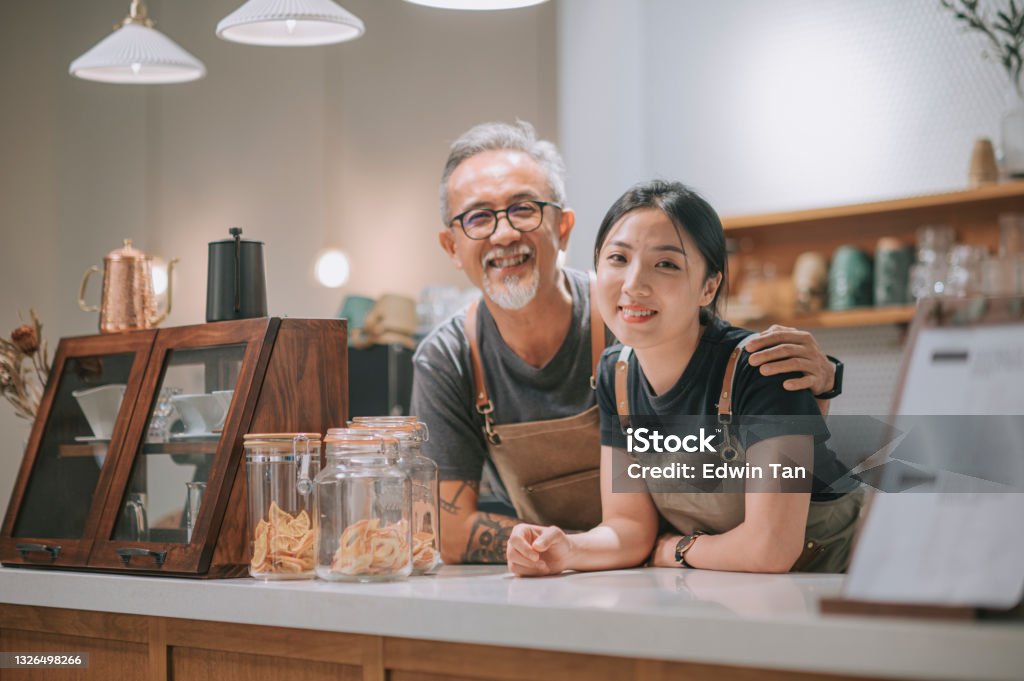 asian chinese senior male cafe owner and her daughters looking at camera smiling at coffee shop counter Small Business Stock Photo